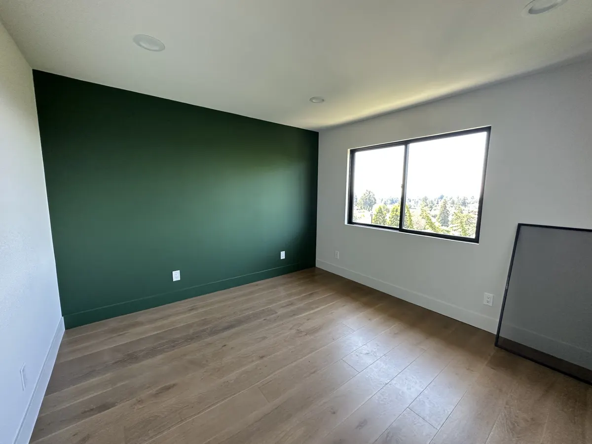 Room with a deep green accent wall and light oak floors