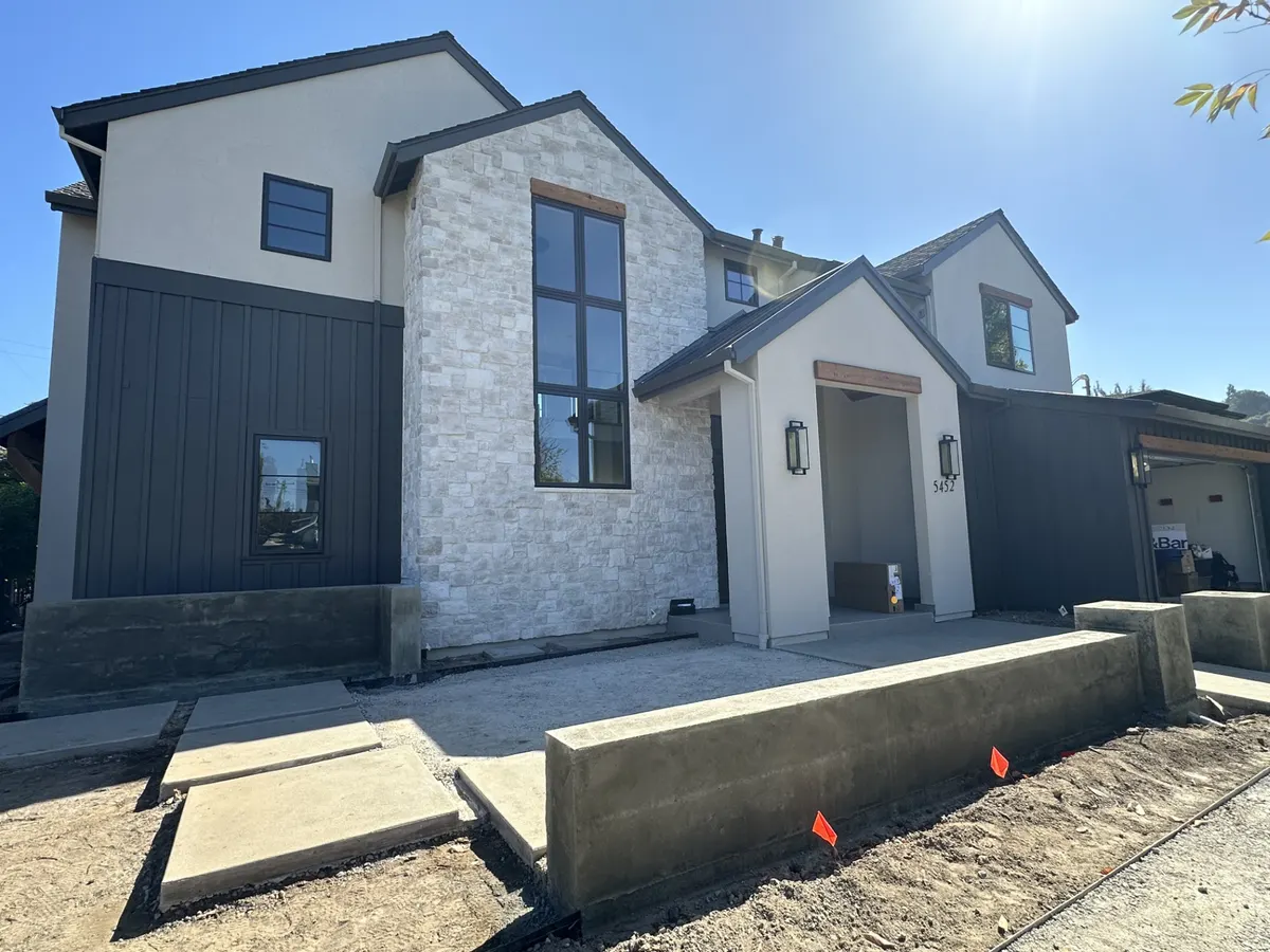 Two-story home with dark board and batten siding, white stucco, and stone