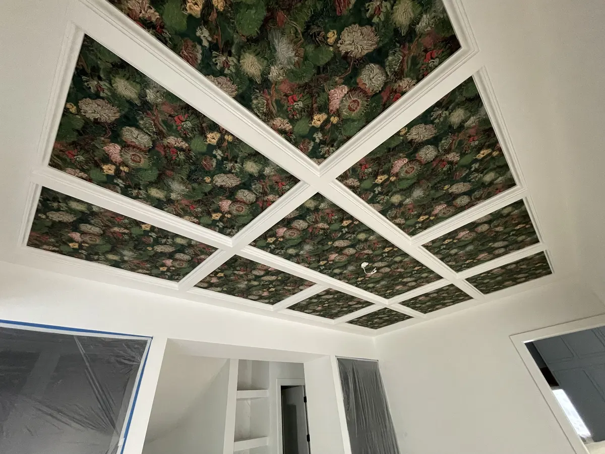 Coffered ceiling panels covered in dark floral wallpaper above a bright white room