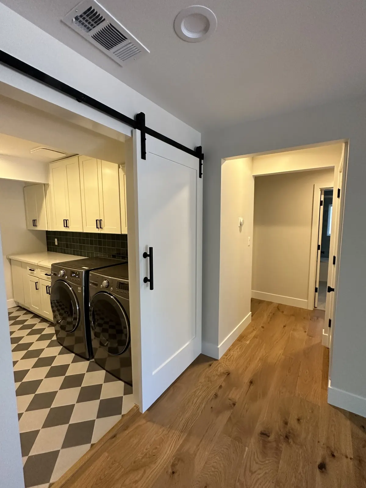 Hallway with a white sliding barn door opening to a laundry room with a checkered floor