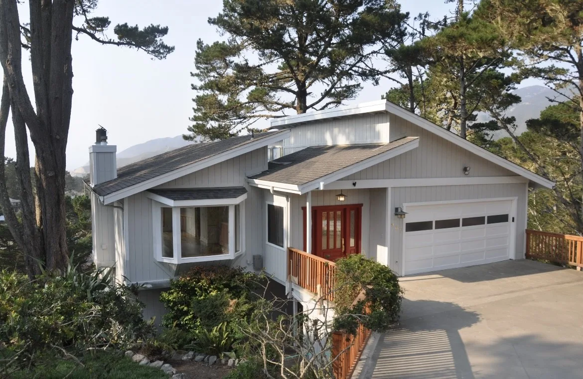 Hillside home painted white with a wood front stair and trees
