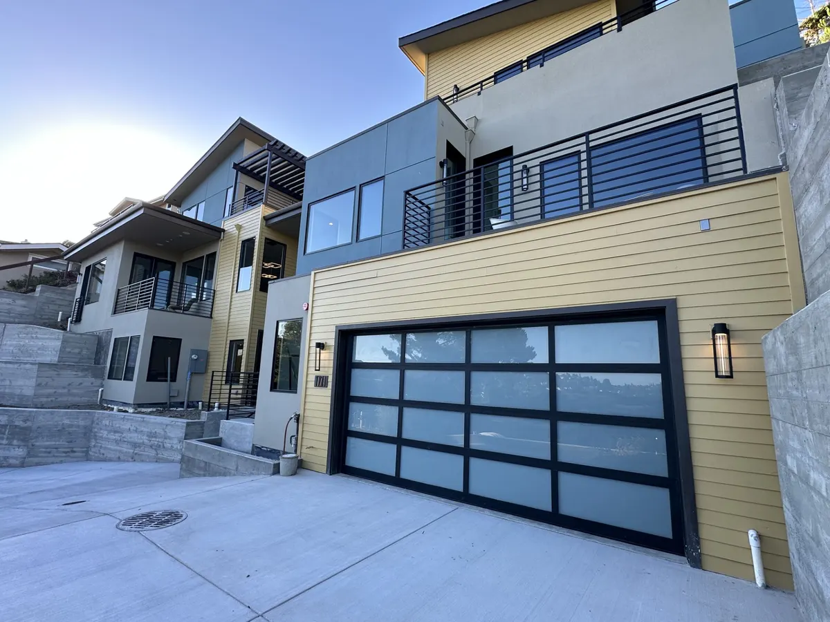 Modern hillside home with yellow siding, dark trim, and a glass garage door