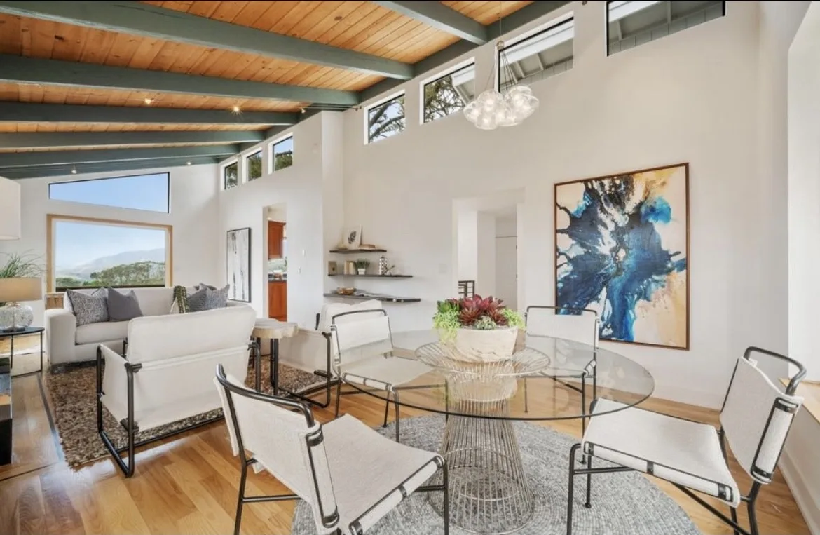 Living room under a stained wood ceiling with white walls and large windows