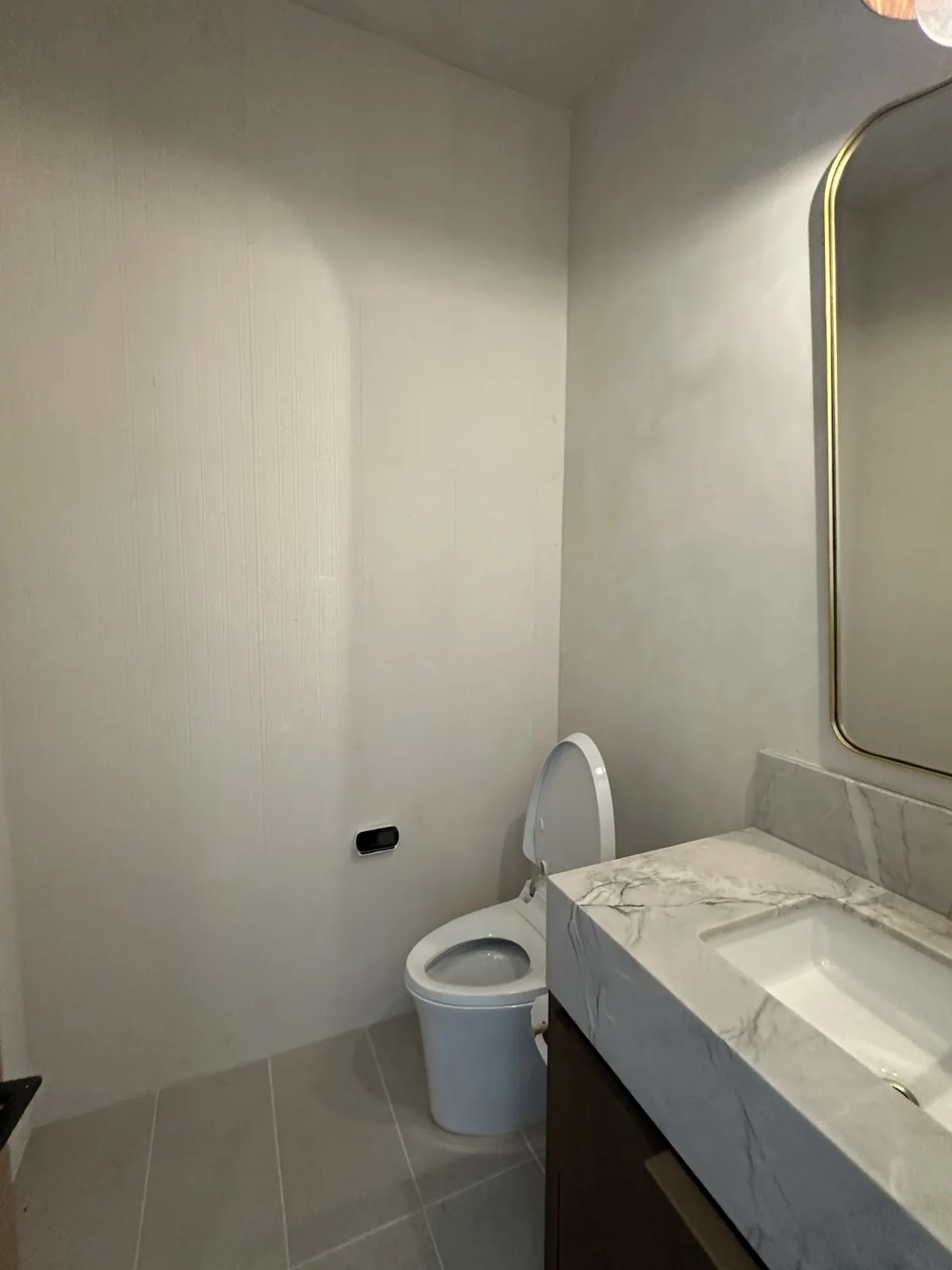 Powder room with soft limewashed walls, a marble vanity, and a round mirror