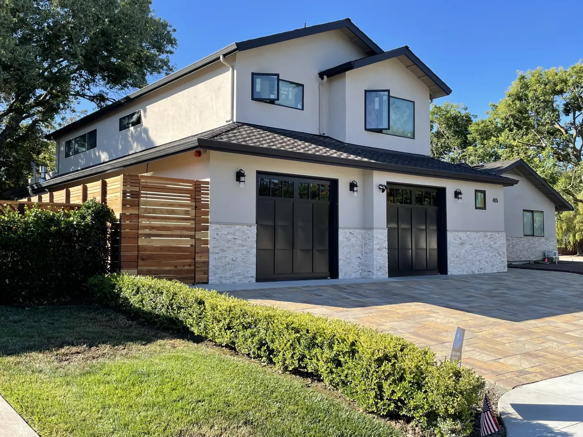Modern farmhouse with white siding, a black roof, and a wood fence