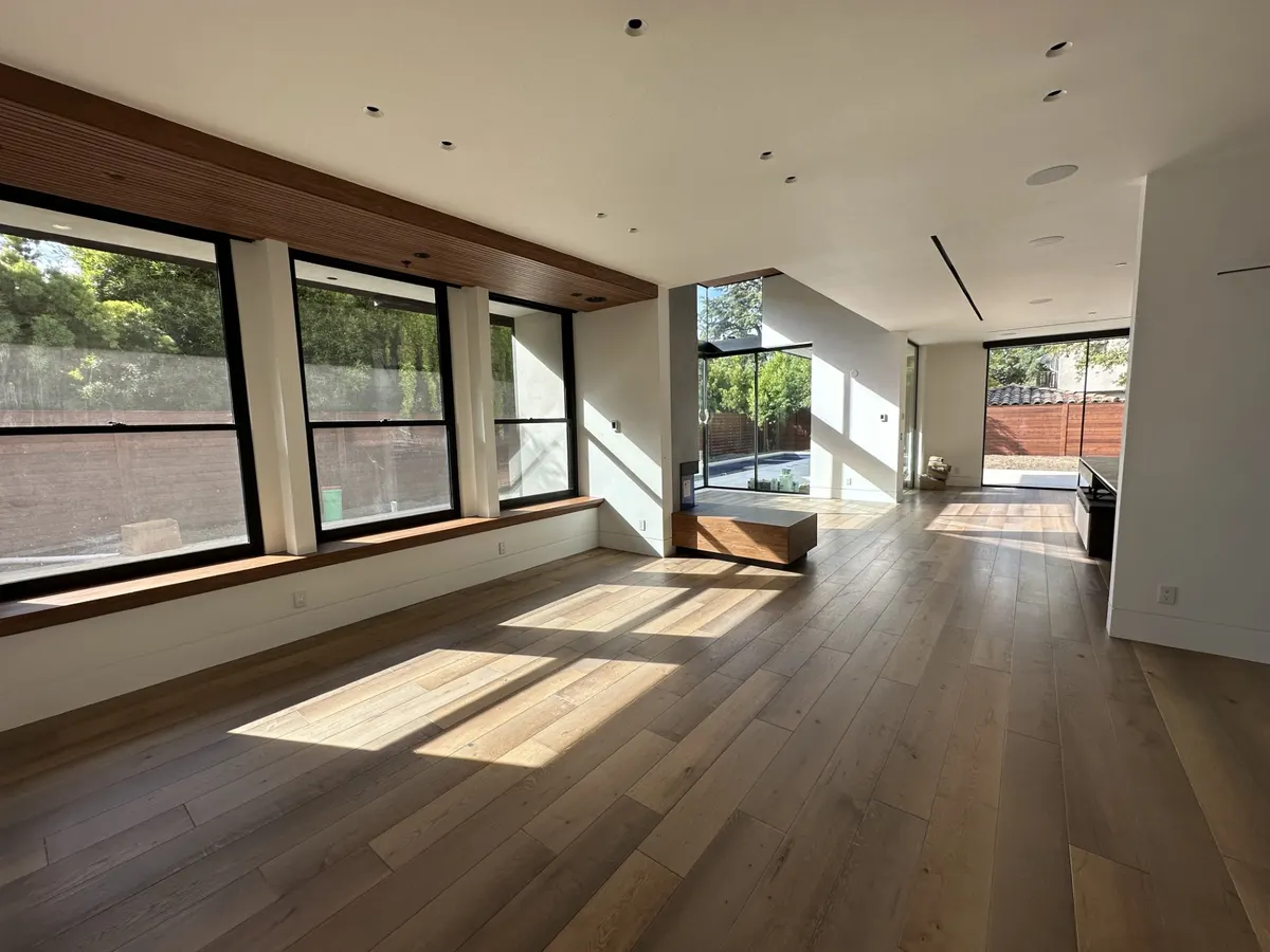 Open-plan room with walnut floors, white walls, and a floating staircase