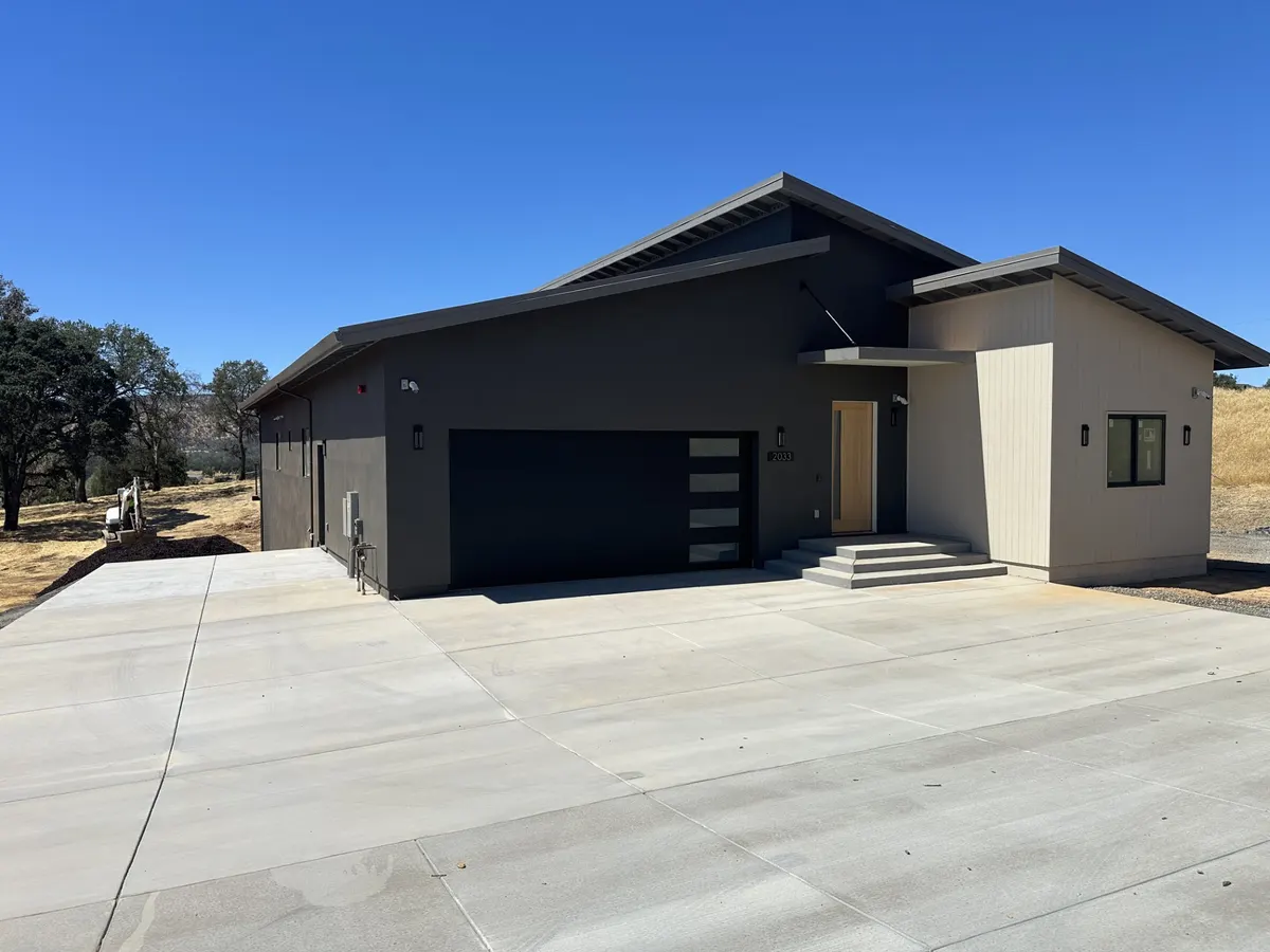 Single-story modern home painted dark gray with a black garage door