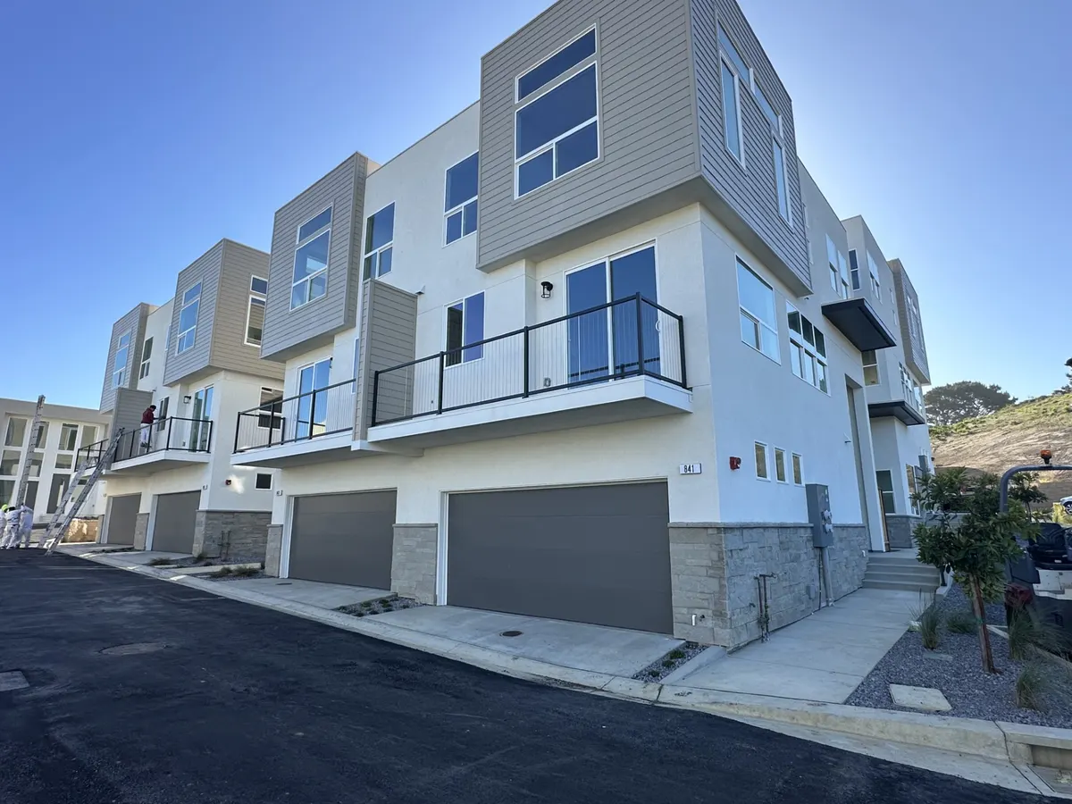 Row of new three-story townhomes with white and gray siding and dark garage doors