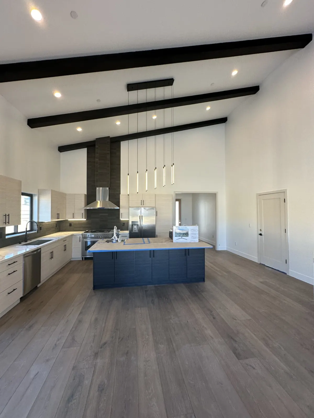 Open kitchen and great room with black ceiling beams, a tiled fireplace, and wood floors