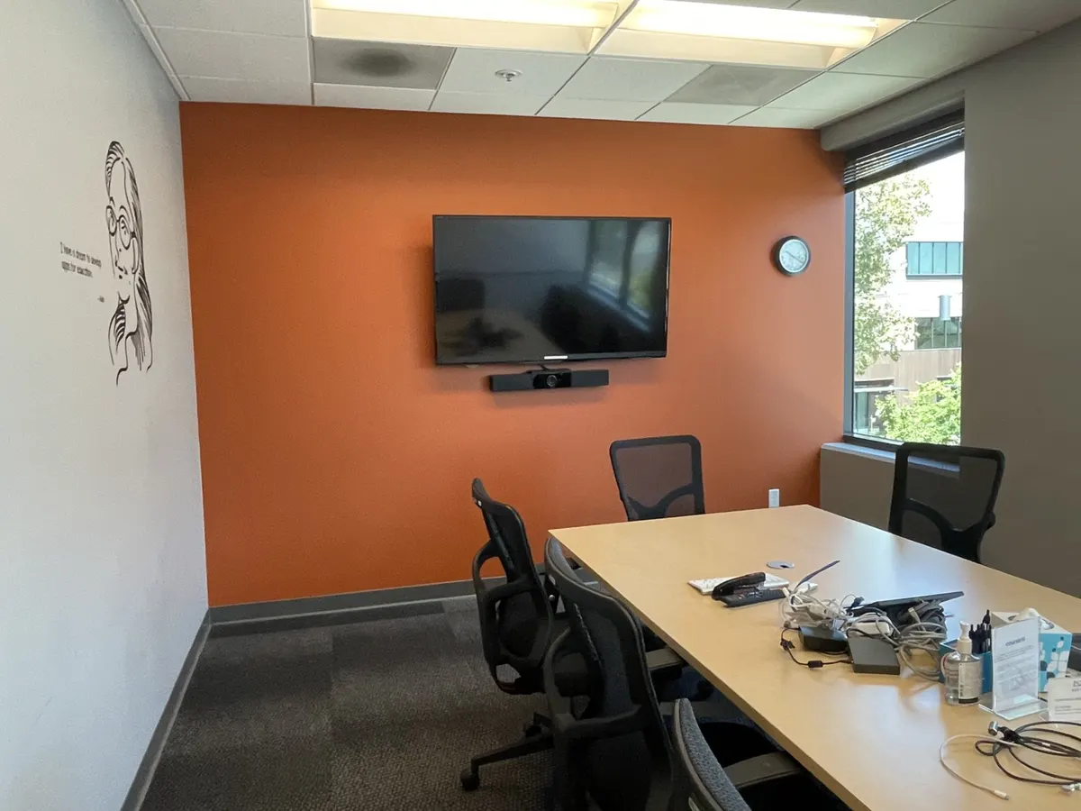 Office conference room with an orange accent wall and a wall-mounted screen