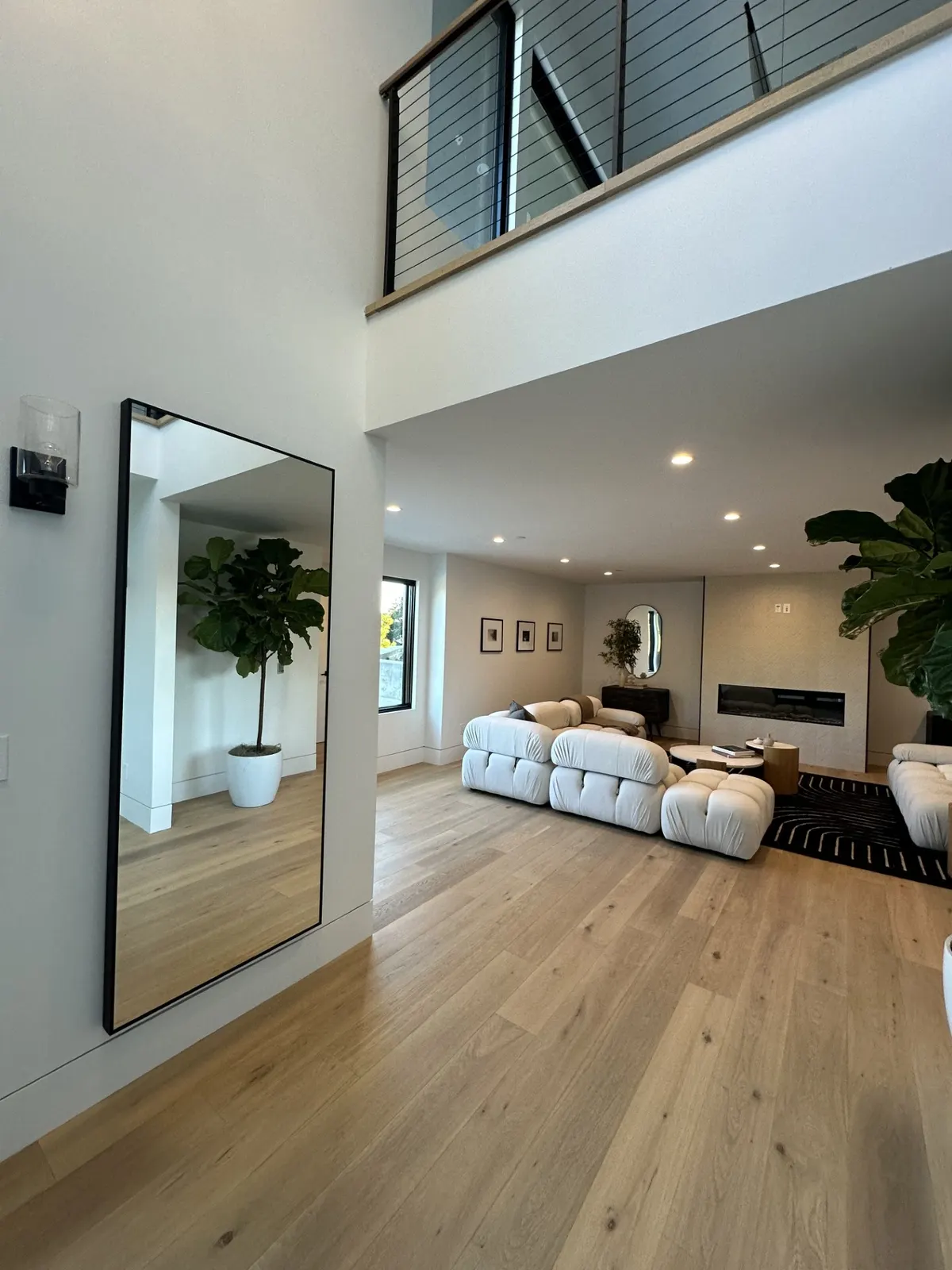 Bright open living room with a white sofa, oak floors, and a loft with a black railing