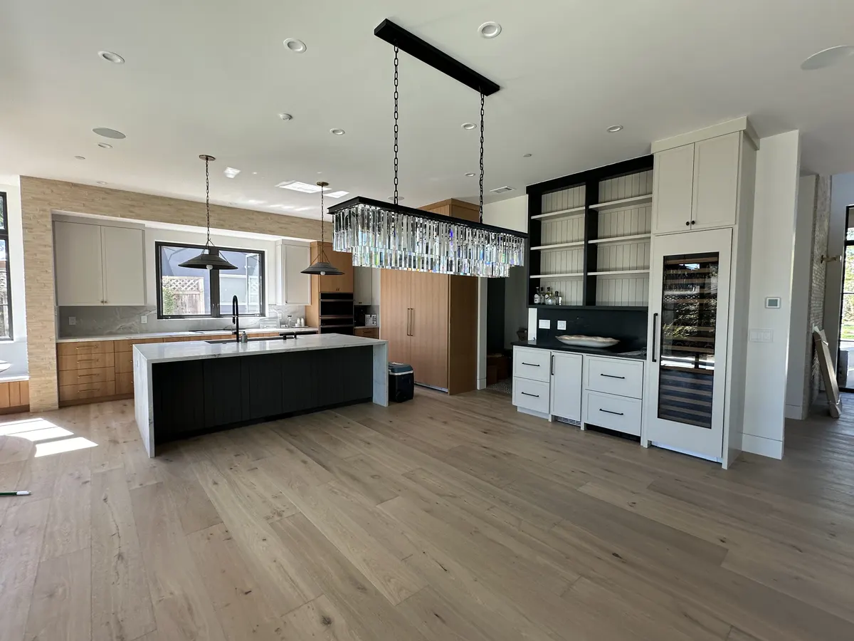 Finished open-plan kitchen with a black island and chandeliers after drywall and paint