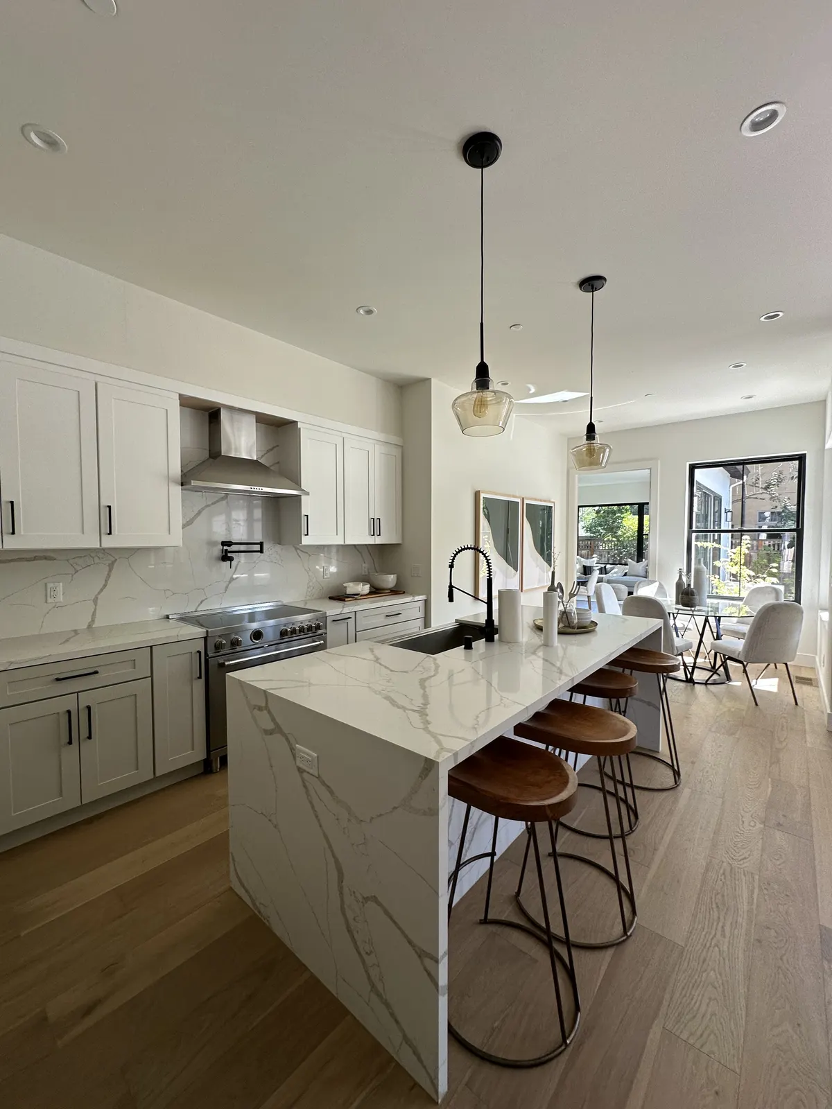 Finished kitchen with a white waterfall island and pendant lights after drywall and paint