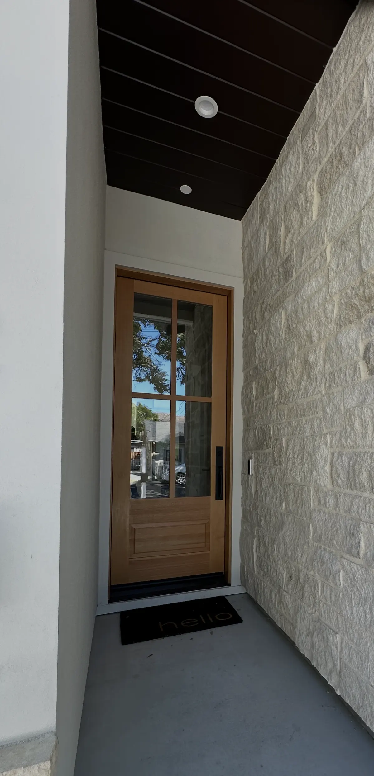 Stained wood front door beneath a dark stained entry ceiling beside stone cladding