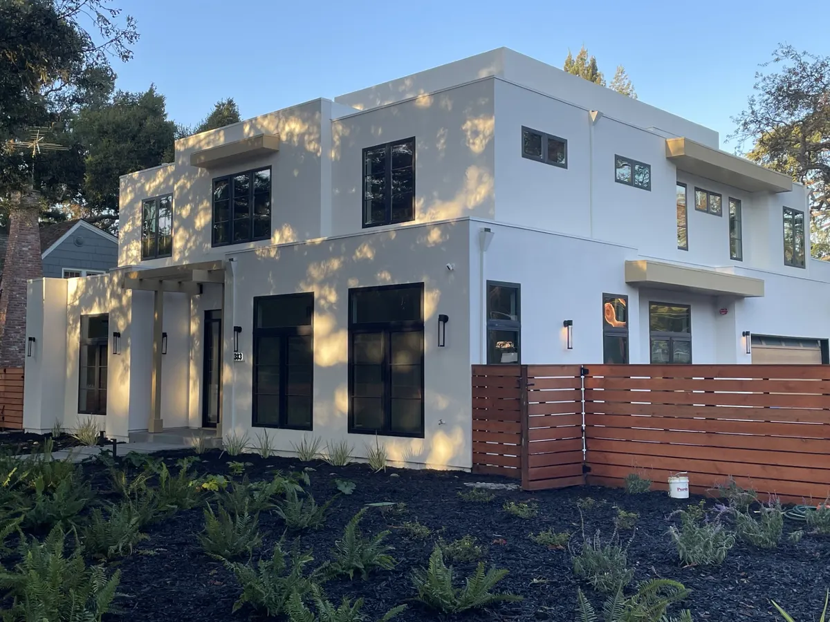 Two-story white stucco home with black windows and a horizontal wood fence